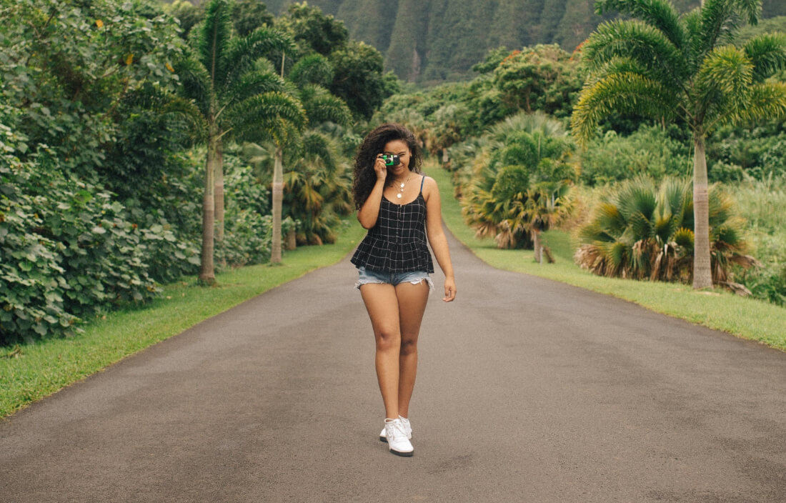 Woman walking toward the camera on a paved road and holding a camera